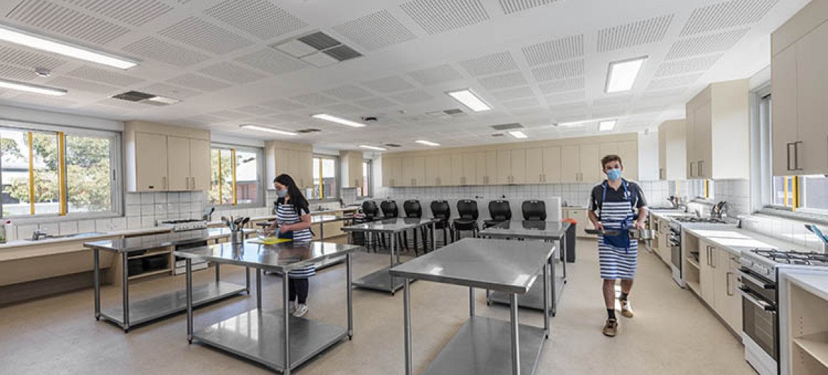 Interior Home Economics Classroom with Steel Benches, Cookware and Two Students in Aprons